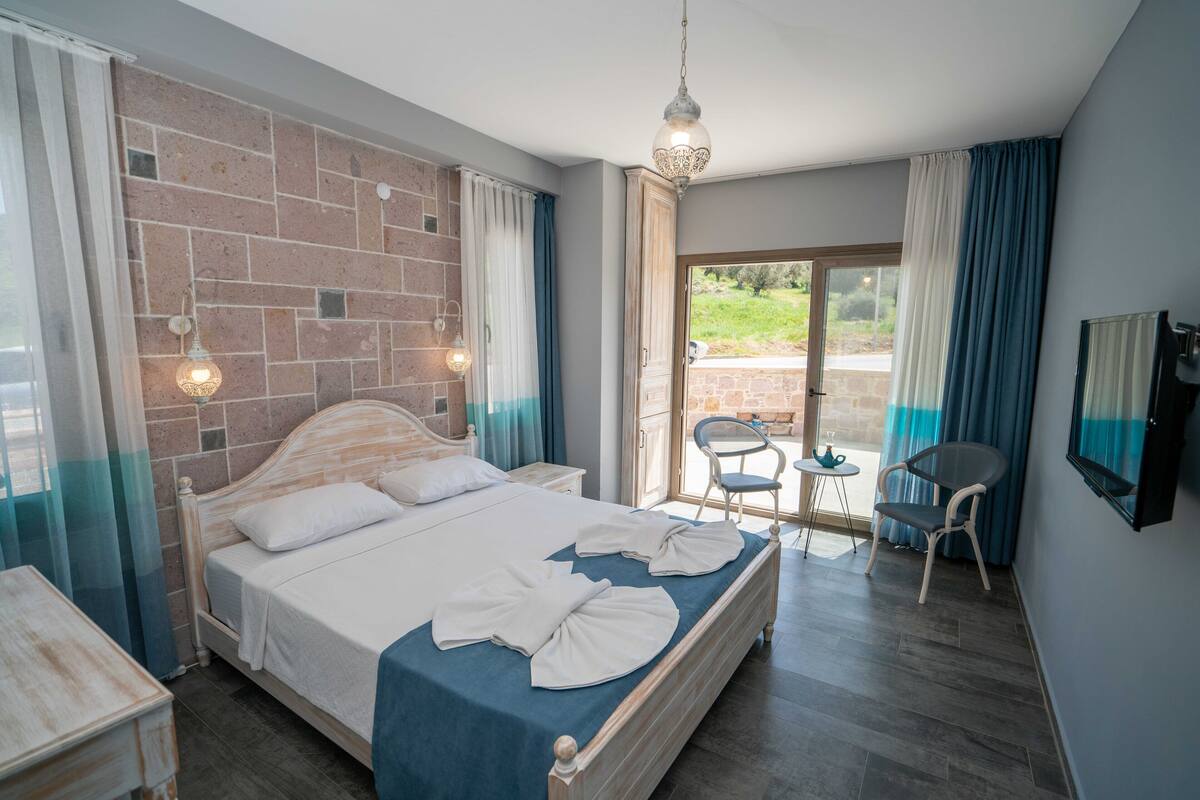 Un dormitorio con una cama, una mesita, sillas, televisor y vistas al exterior.