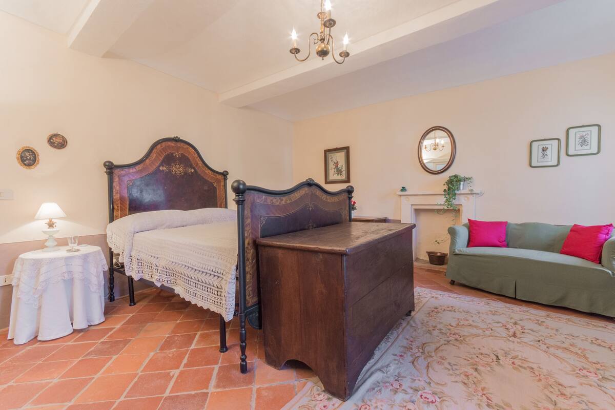 A bedroom with a wooden bed, a green sofa, a small table with a lamp, and a fireplace.