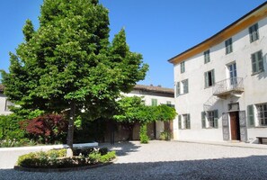 A courtyard with a large tree, a building with green shutters, and a gravel ground.