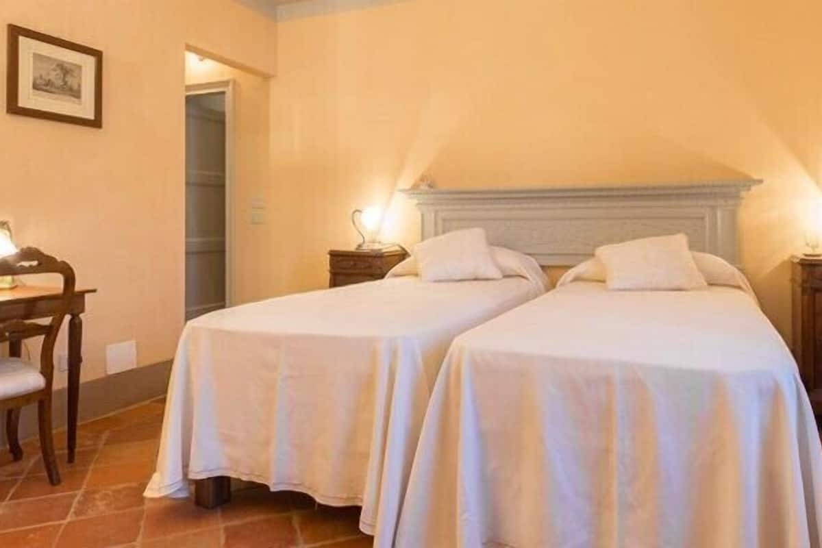 A hotel room with two single beds, a desk, and a chair.