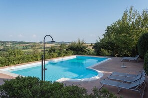 A swimming pool with a curved edge, surrounded by lounge chairs and a view of the countryside.