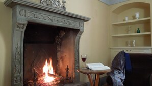 A fireplace with a fire, a glass of red wine, and a book on a small table.