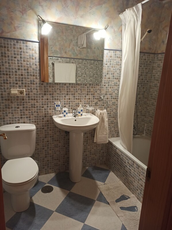 A bathroom with a toilet, sink, and bathtub. There is a mirror above the sink and a towel hanging on the wall. The floor has a checkered pattern.