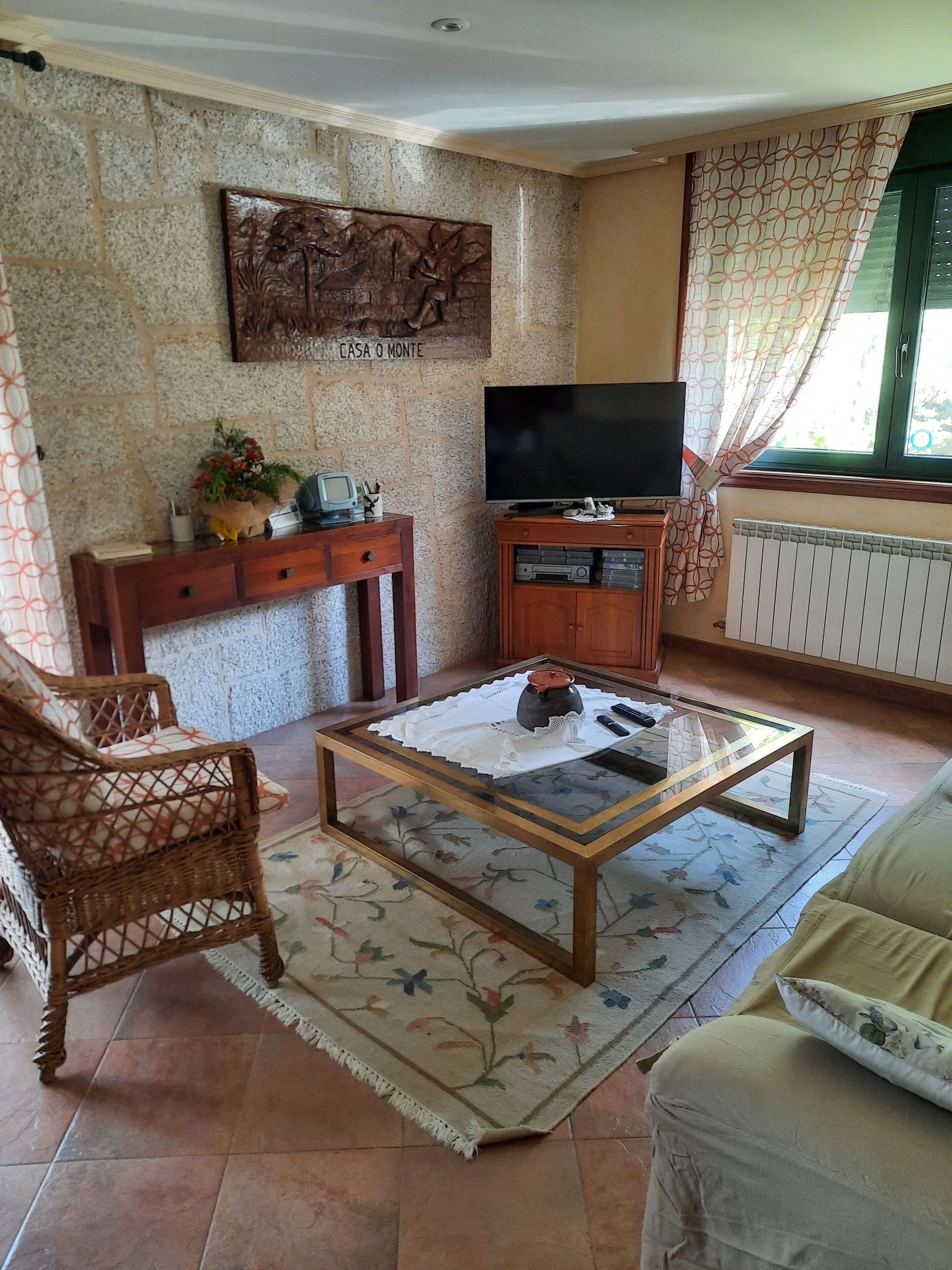 Ein Wohnzimmer mit Fernseher, Couchtisch, Korbsessel, Sofa und einer Wanddekoration.