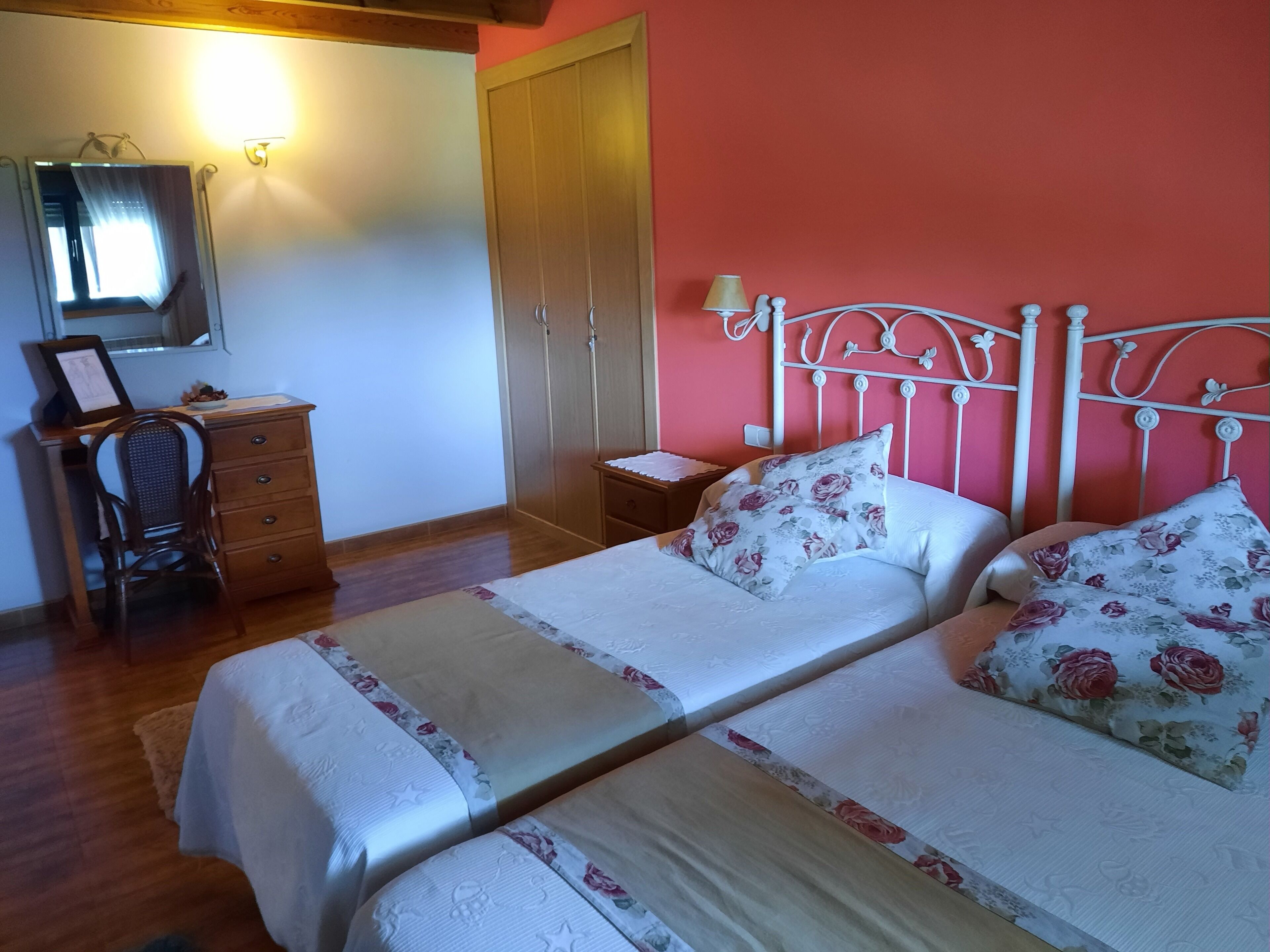 A bedroom with two beds, a wooden desk, a chair, a wardrobe, and a mirror.