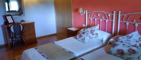 A bedroom with two beds, a wooden desk, a chair, a wardrobe, and a mirror.
