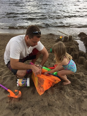 A man and a child on a sandy beach, engaged in building sand structures.