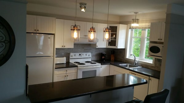 A kitchen with white cabinets, a black countertop, a stove, and a sink. There are pendant lights above the counter.
