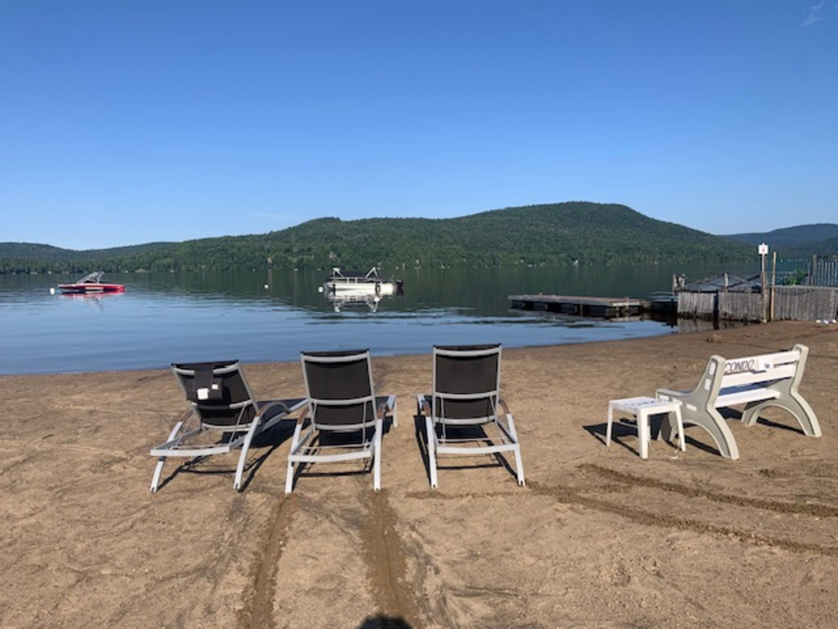 A beach with lounge chairs and a dock with boats.