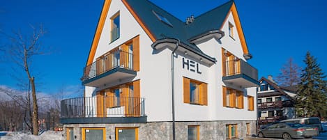 A multi-story hotel with a modern design, featuring balconies, a stone facade, and a ski lift in the background.