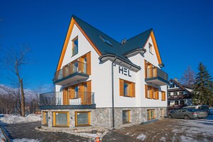 A multi-story hotel with a modern design, featuring balconies, a stone facade, and a ski lift in the background.