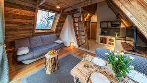 A cozy loft-style room with a wooden ceiling, a loft bed, a dining area with a table set for two, and a kitchenette in the background. - Hel Apartments (Zakopane)
