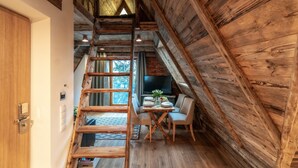 A rustic wooden interior with a loft dining area, wooden staircase, and a television. - Hel Apartments (Zakopane)