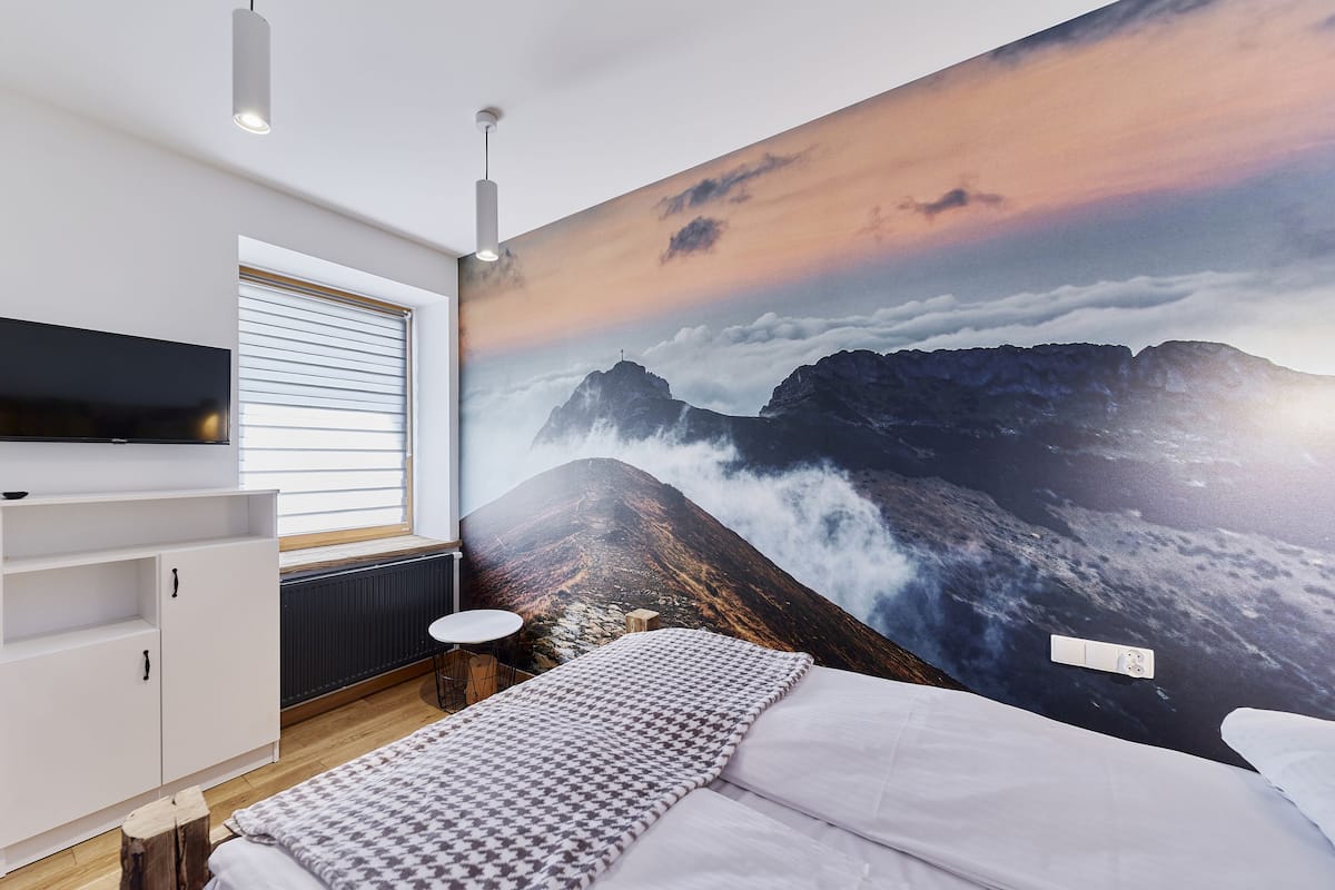 Un dormitorio moderno con un gran mural de montañas, un televisor de pantalla plana, un armario de madera y una mesa redonda.