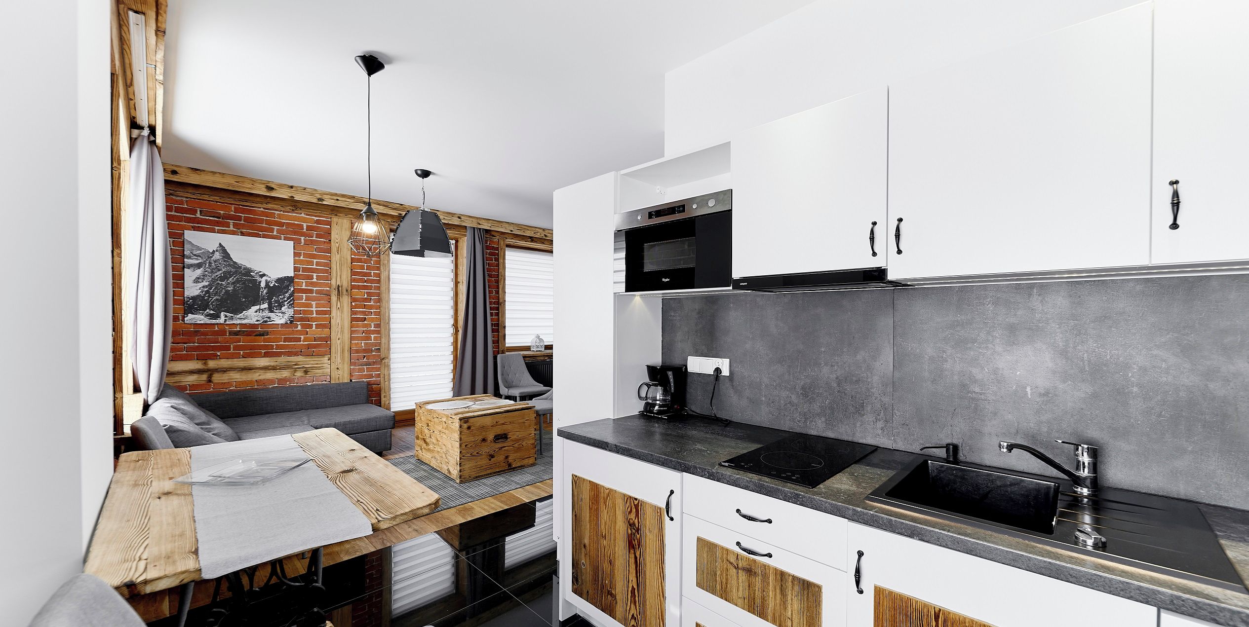 A compact kitchen with white cabinets, a black countertop, and a wooden table.