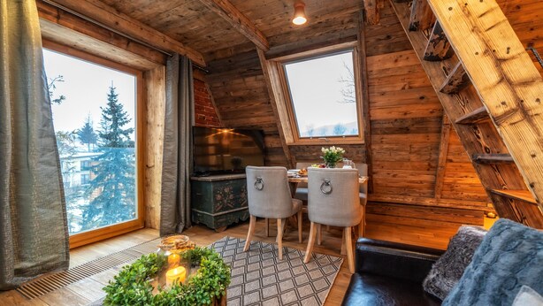 A cozy cabin interior with a dining area, a fireplace, and a view of trees through large windows. - Hel Apartments (Zakopane)