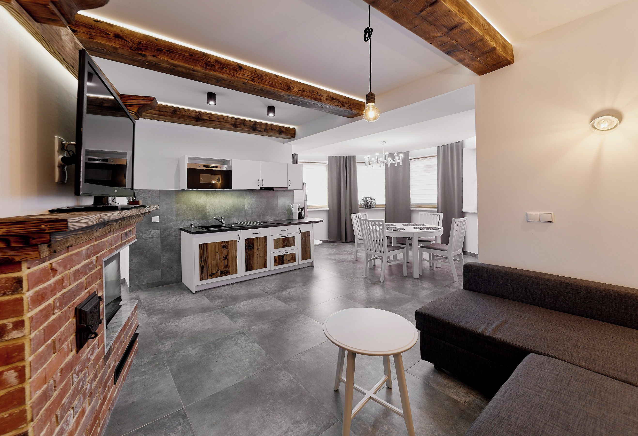 Una cocina moderna con una isla central, un comedor con candelabro y una sala de estar con sofá y taburete.