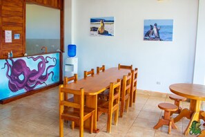 A wooden dining table with chairs, a blue water dispenser, and a mural of an octopus on the wall.