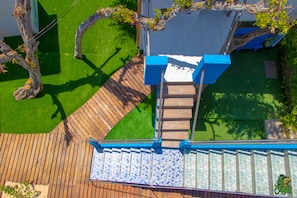 Una terraza de madera con barandilla azul, zona empavedada y césped verde.
