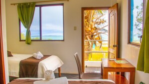 Une chambre d’hôtel avec deux lits, un bureau en bois et une vue sur l’océan par une grande fenêtre.