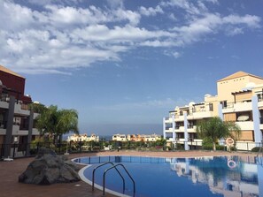 Una piscina sota un cel serè, envoltada d'edificis alts amb balcons.