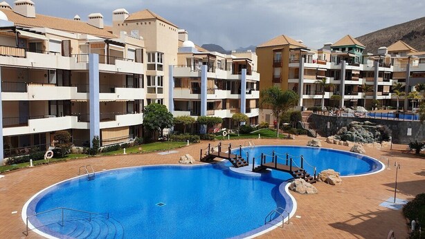 Hotel amb múltiples balcons, una piscina central i un paisatge de muntanyes al fons.