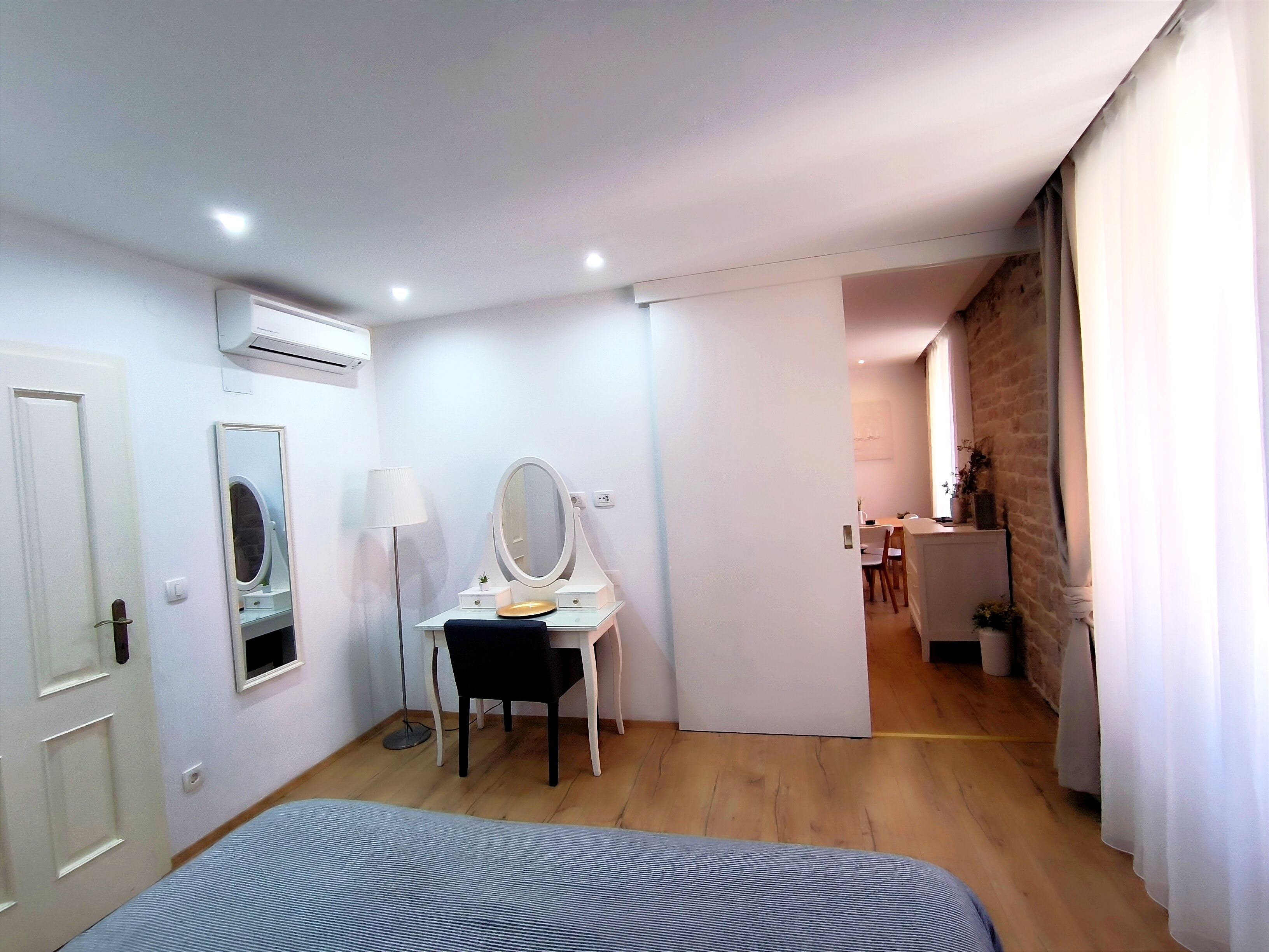 Une chambre à coucher avec un lit, un bureau doté d’un miroir, une lampe et une petite fenêtre.