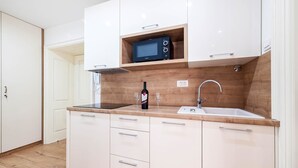 A modern kitchen with white cabinets, a wooden countertop, a built-in microwave, a wine bottle, and two wine glasses. - Rialto Luxury Apartment (Sibenik)