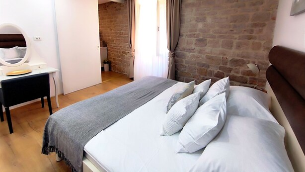 A bedroom with a bed, a desk with a mirror, a dresser, and a brick wall. - Rialto Luxury Apartment (Sibenik)
