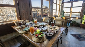 A wooden dining table set with various food items and beverages, surrounded by large windows offering a view of a mountainous landscape. - Royal Cave Hotel (Ürgüp)