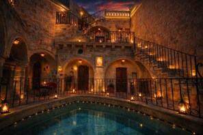 A stone building with a pool, arched doorways, and a staircase leading to a balcony. - Royal Cave Hotel (Ürgüp)