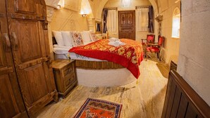 A traditional room with a bed, wooden furniture, and stone walls. - Royal Cave Hotel (Ürgüp)