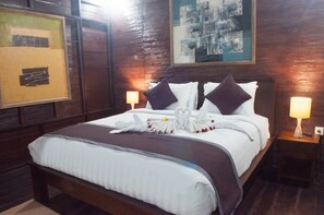 A hotel room with a large bed, two bedside tables with lamps, wooden paneling, and artwork on the walls.