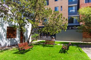 A courtyard with two benches, a tree, and a building with multiple windows. - GIO Suites Bogota (Bogotá)