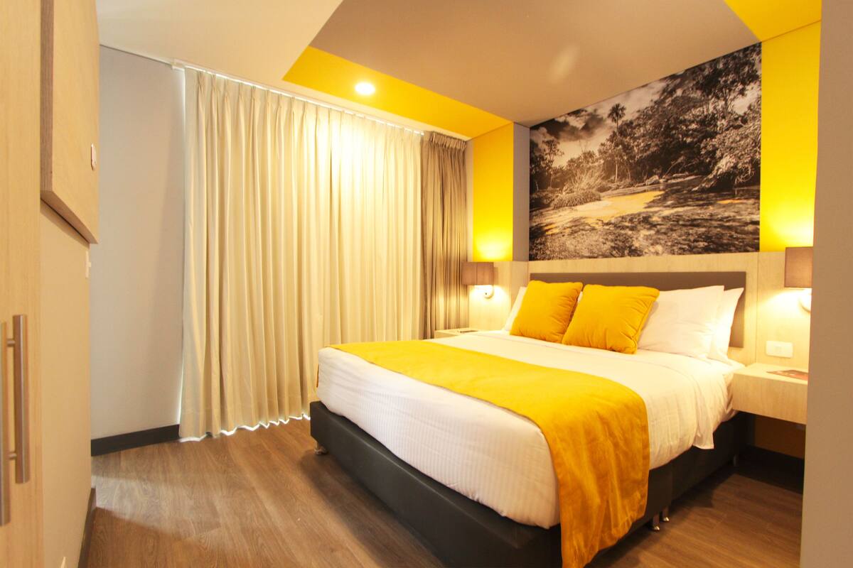 A hotel room with a large bed, curtains, a nightstand, and a wall-mounted lamp.