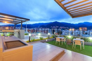 An outdoor terrace with a view of a cityscape and mountains, featuring a sink, a planter, and seating areas. - GIO Suites Bogota (Bogotá)