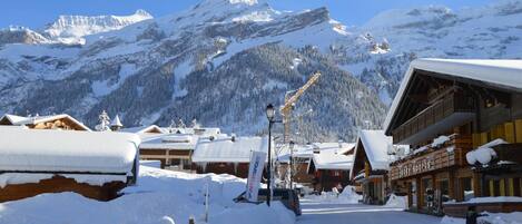 A snow-covered mountain town with wooden buildings, a ski lift, and a clear blue sky.