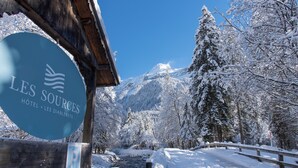 A sign for Les Sources Hotel with a view of snow-covered mountains and a river. - Hôtel Les Sources (Ormont-Dessus)