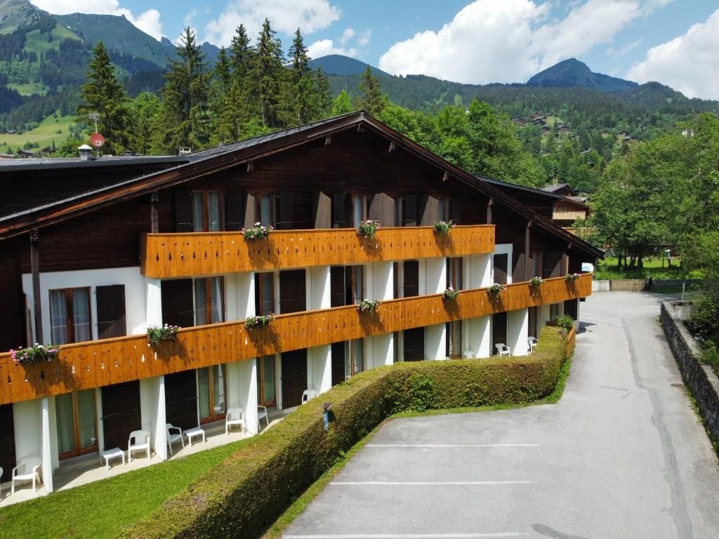 Een hotel met een houten gevel, balkons met planten en uitzicht op bergen.