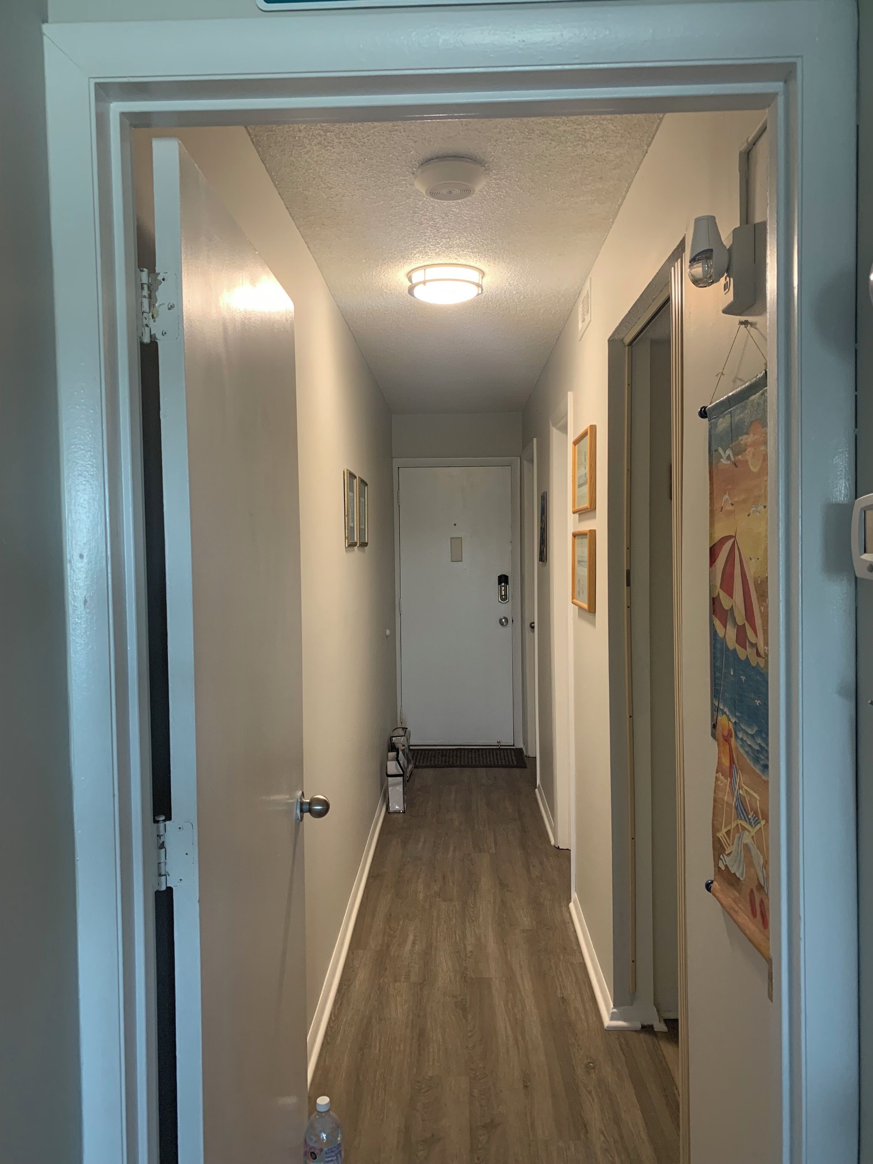 A hallway with wooden flooring, white walls, and a door at the end.