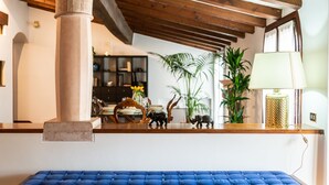 Une pièce avec un plafond en bois, un banc bleu rembourré, une bibliothèque et une lampe.