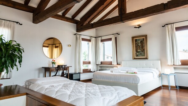Une chambre avec deux lits, des poutres en bois, un grand miroir, un tableau et une plante en pot.