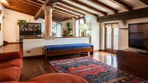 Un salon chaleureux avec un plafond en bois, un lit recouvert d’une couverture bleue, un canapé rouge et un tapis à motifs.