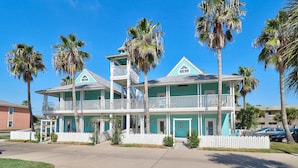 A two-story house with a balcony, surrounded by palm trees and a white picket fence. - Seashell Village Resort near the beach with kitchens (Port Aransas)