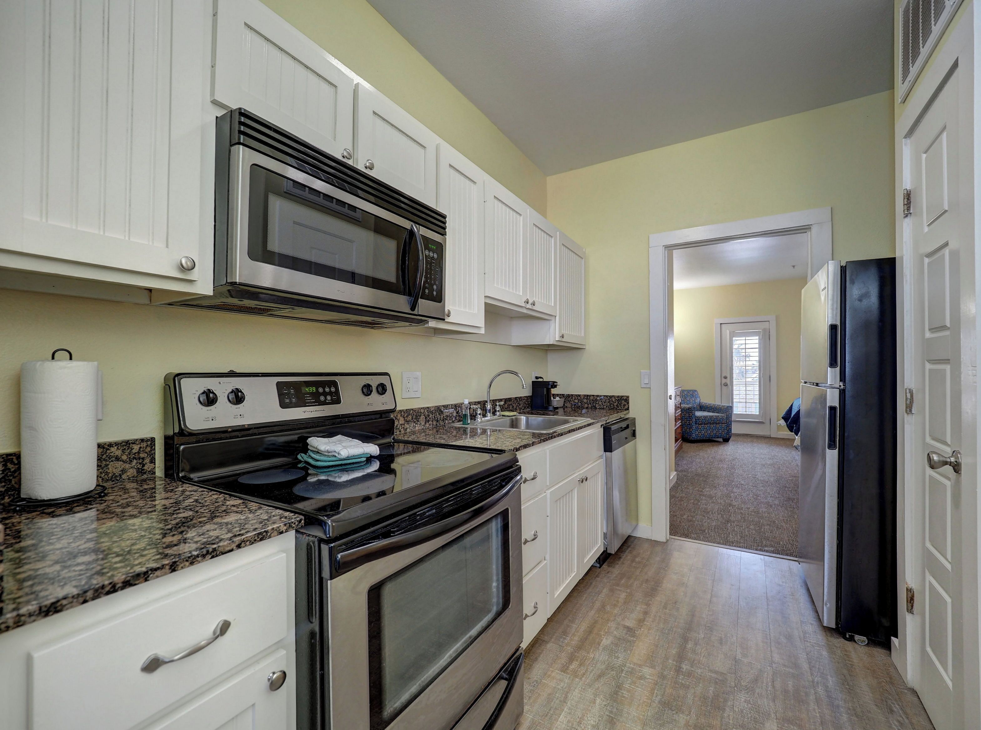 A kitchen with white cabinets, a microwave, an oven, a sink, and a refrigerator.