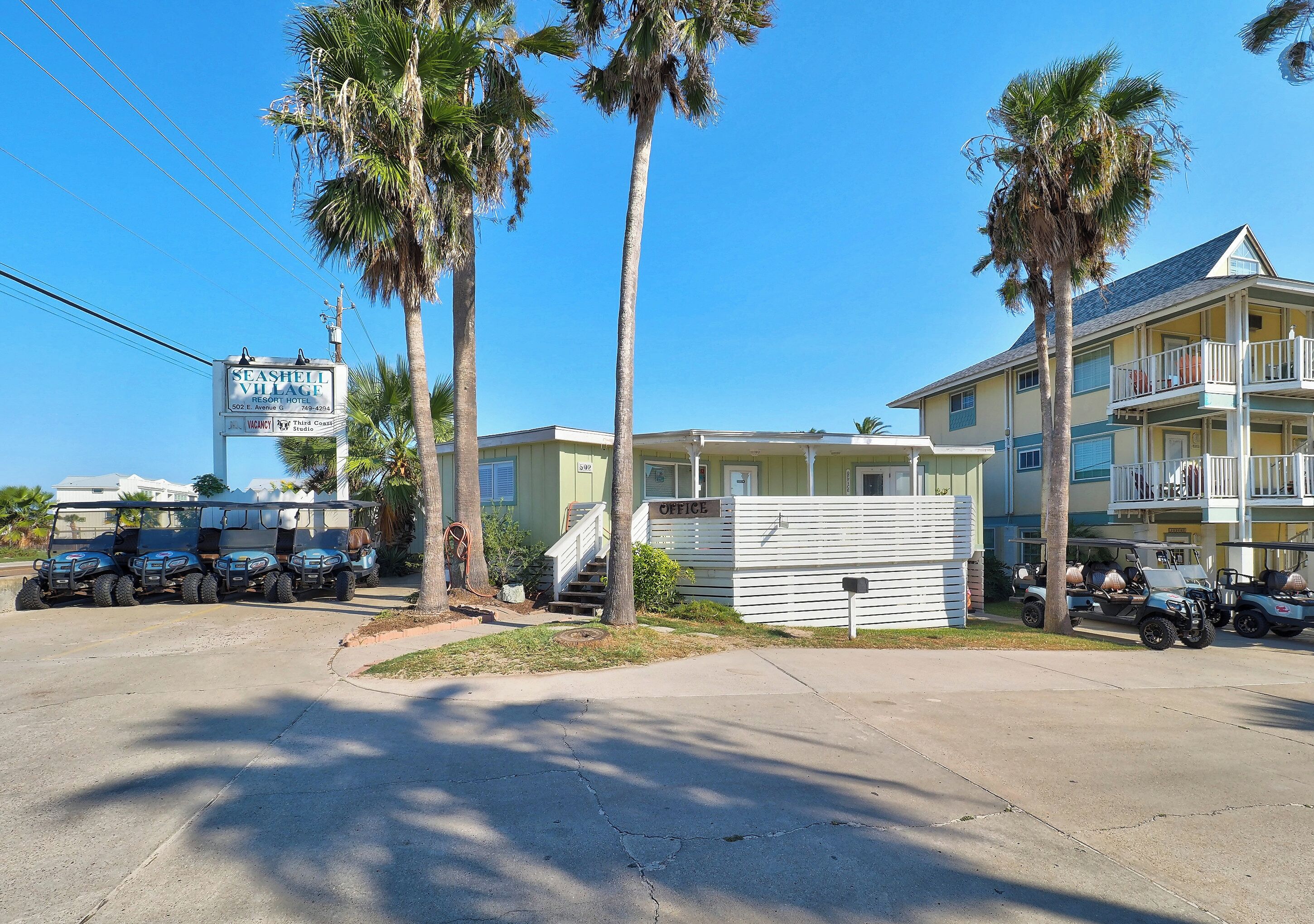 A resort hotel with a signboard, multiple vehicles, and a two-story building with a balcony.