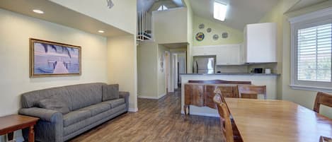 A spacious living area with a gray sofa, wooden dining table, and chairs. A ceiling fan and recessed lighting are visible.