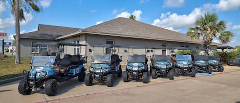 A row of golf carts parked in front of a building with a sloped roof and windows.