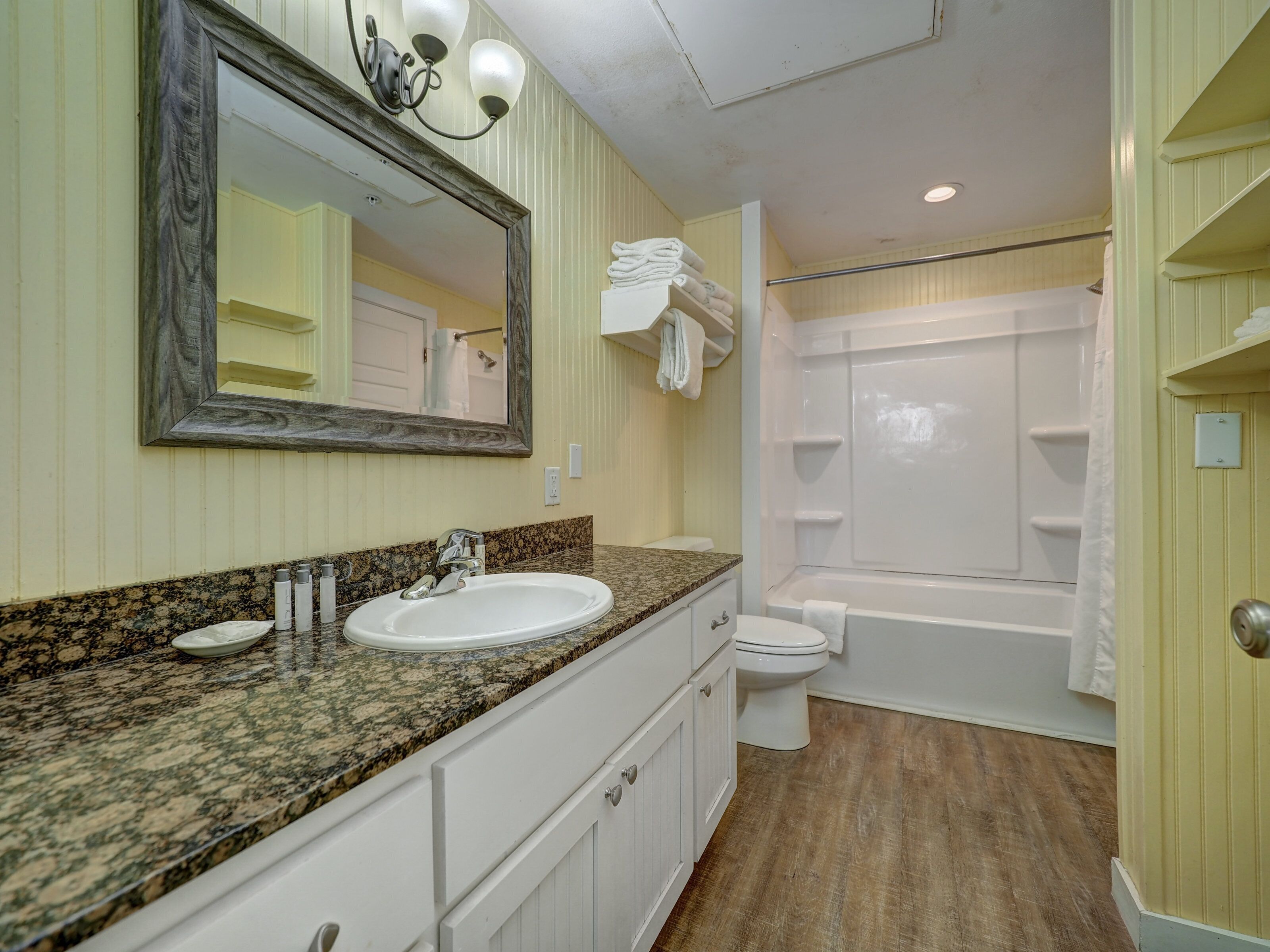 Baño con lavamanos de granito, inodoro blanco, bañera y ducha.