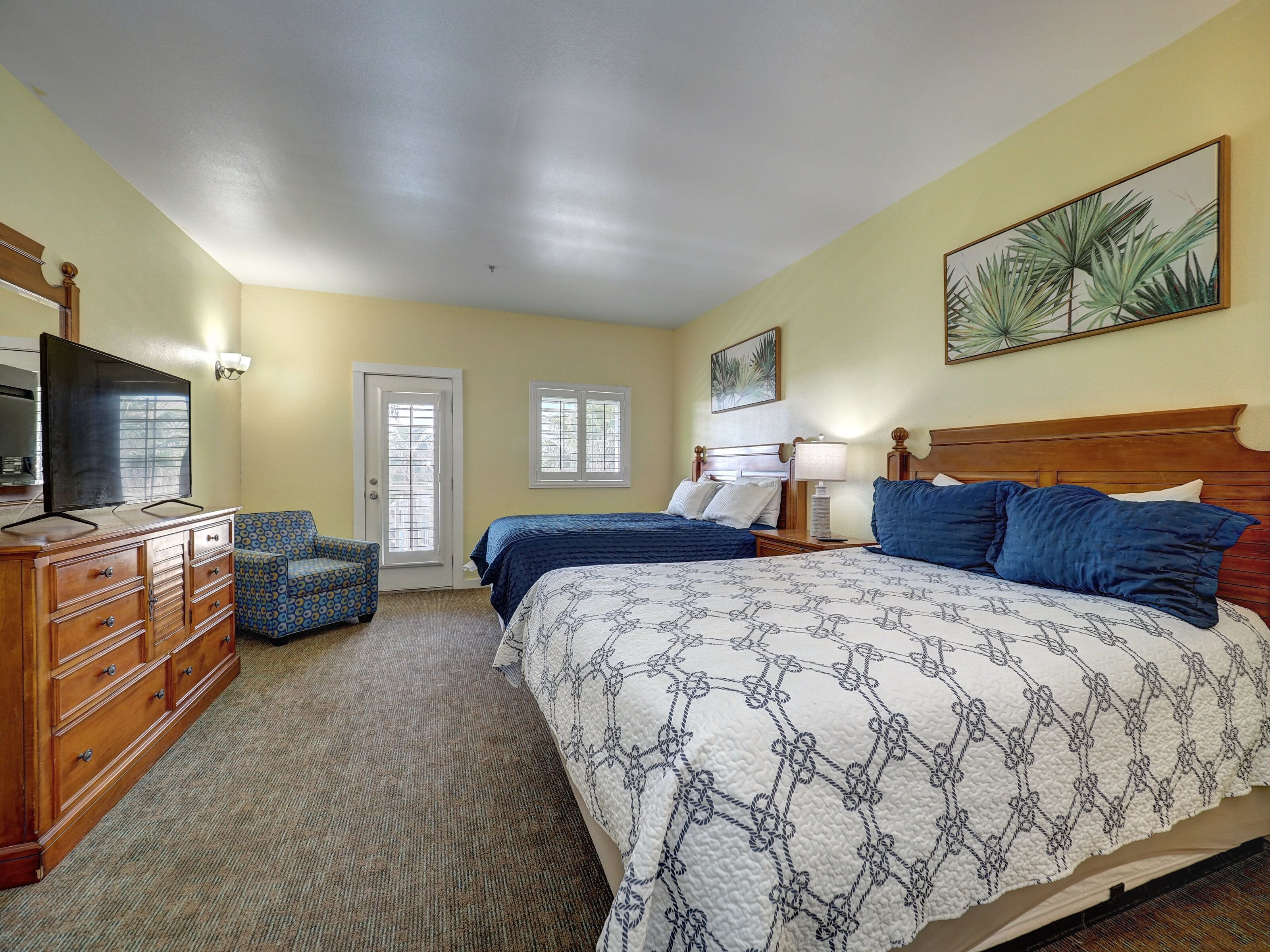 A hotel room with two beds, a wooden dresser, a television, and a door with a window.
